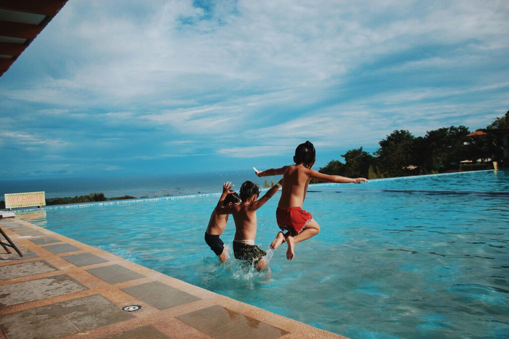 Two children joyfully jump into a pool on a sunny day, embodying excitement and summer vibes.